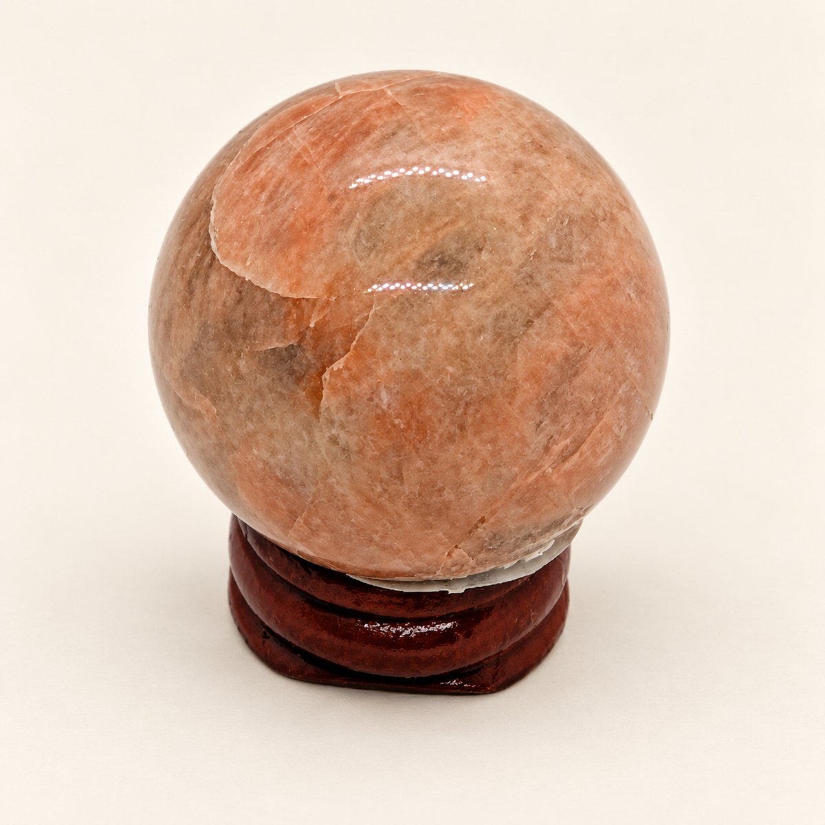 3 cm Peach Moonstone Sphere with peach-pink tones and pale curved markings on a wooden display stand; stand not included