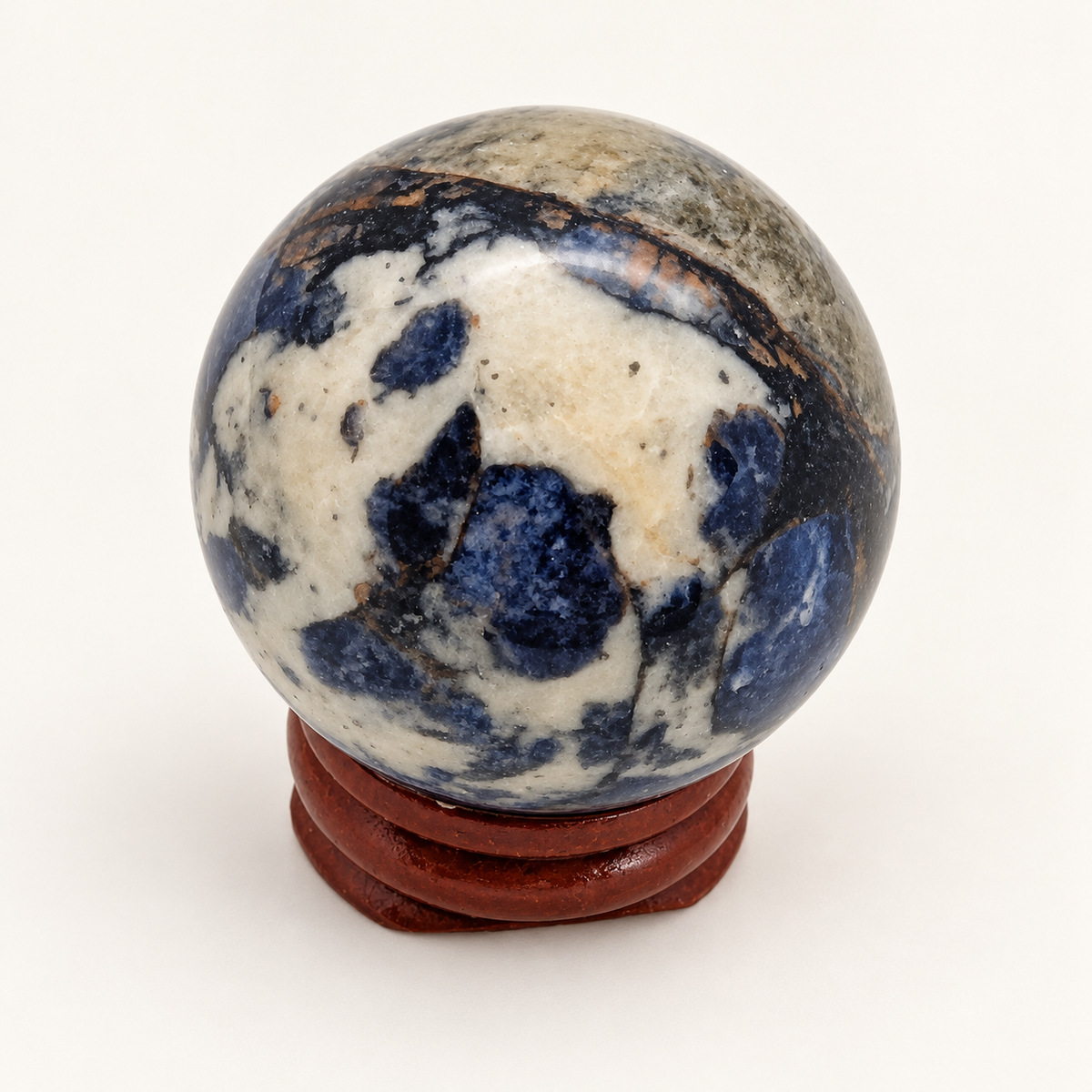 3 cm Blue Sodalite sphere with broad cream areas and navy patches on a wooden display stand