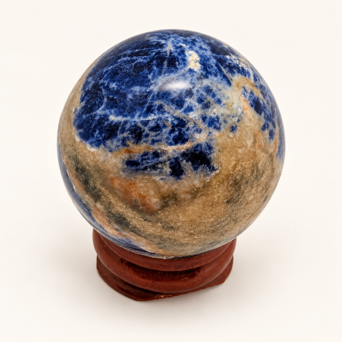 3 cm Blue Sodalite sphere showing a blue upper face and earthy brown and cream areas on a wooden display stand