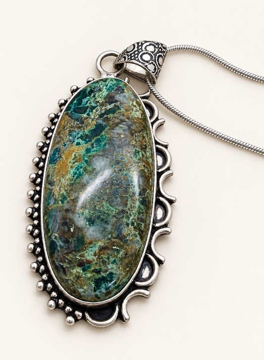 Oval green and teal Chrysocolla pendant in an ornate silver-tone setting with chain on an ivory background