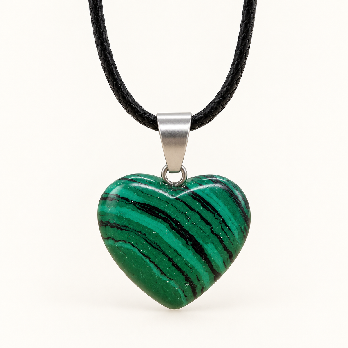 Green heart-shaped Malachite pendant with dark diagonal bands, a silver-tone bail and black cord on an ivory background