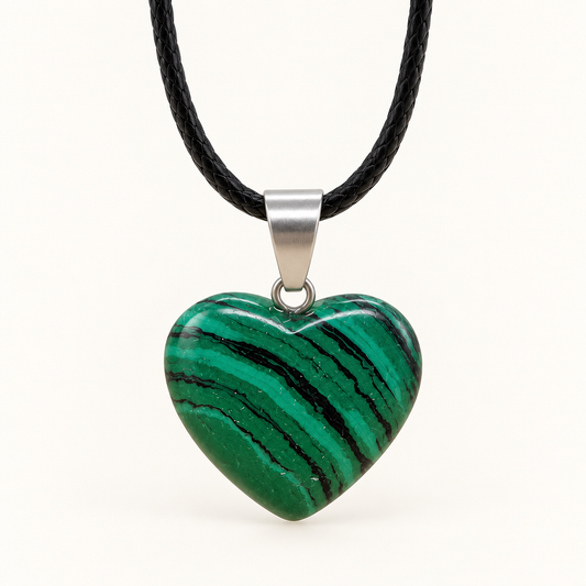 Green heart-shaped Malachite pendant with dark diagonal bands, a silver-tone bail and black cord on an ivory background
