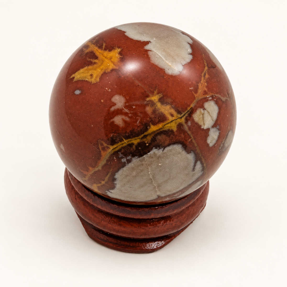 Second view of a polished Noreena Jasper sphere showing grey patches and branching yellow veins against red-brown stone