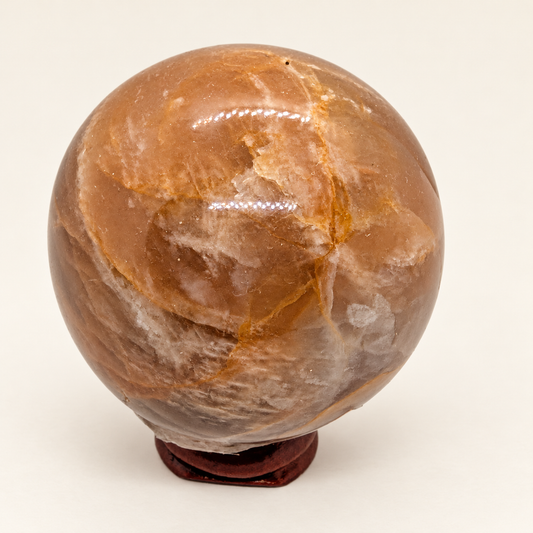 5 cm Peach Moonstone Sphere with peach, brown and cream markings on a wooden display stand; stand not included