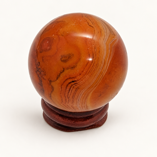 Polished orange-brown Sardonyx sphere with fine curved banding on a wooden display stand against an ivory background