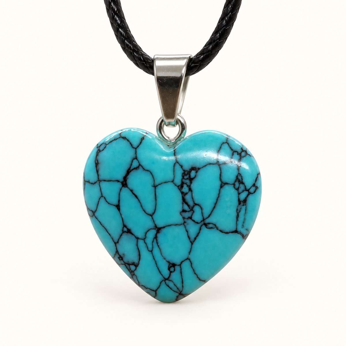 Turquoise-blue heart-shaped Turquenite pendant with dark web-like veining, a silver-tone bail and black cord on an ivory background
