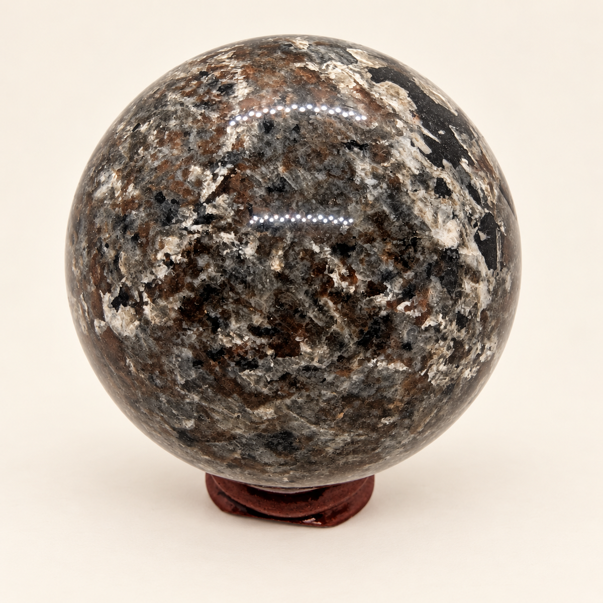 6 cm Yooperlite Sphere with grey, black and cream mottled markings on a wooden display stand in normal lighting; stand not included