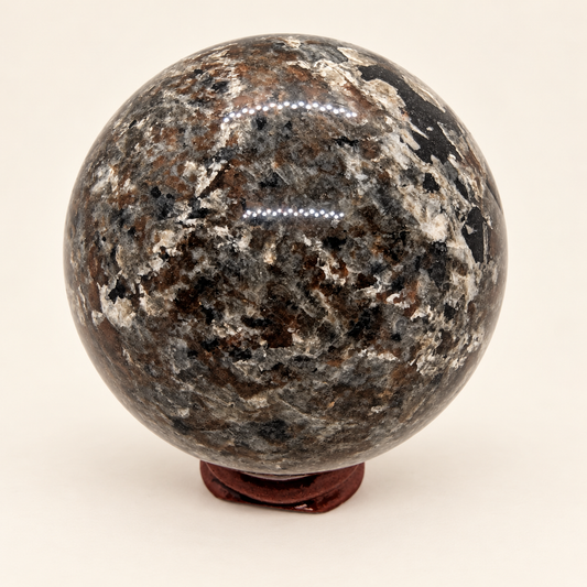 6 cm Yooperlite Sphere with grey, black and cream mottled markings on a wooden display stand in normal lighting; stand not included